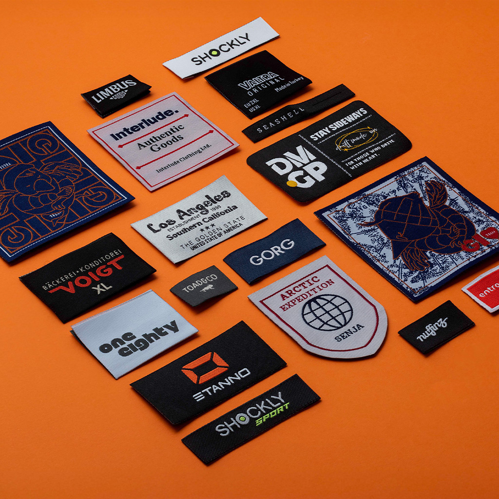 Large assortment of woven clothing labels displayed on orange surface.