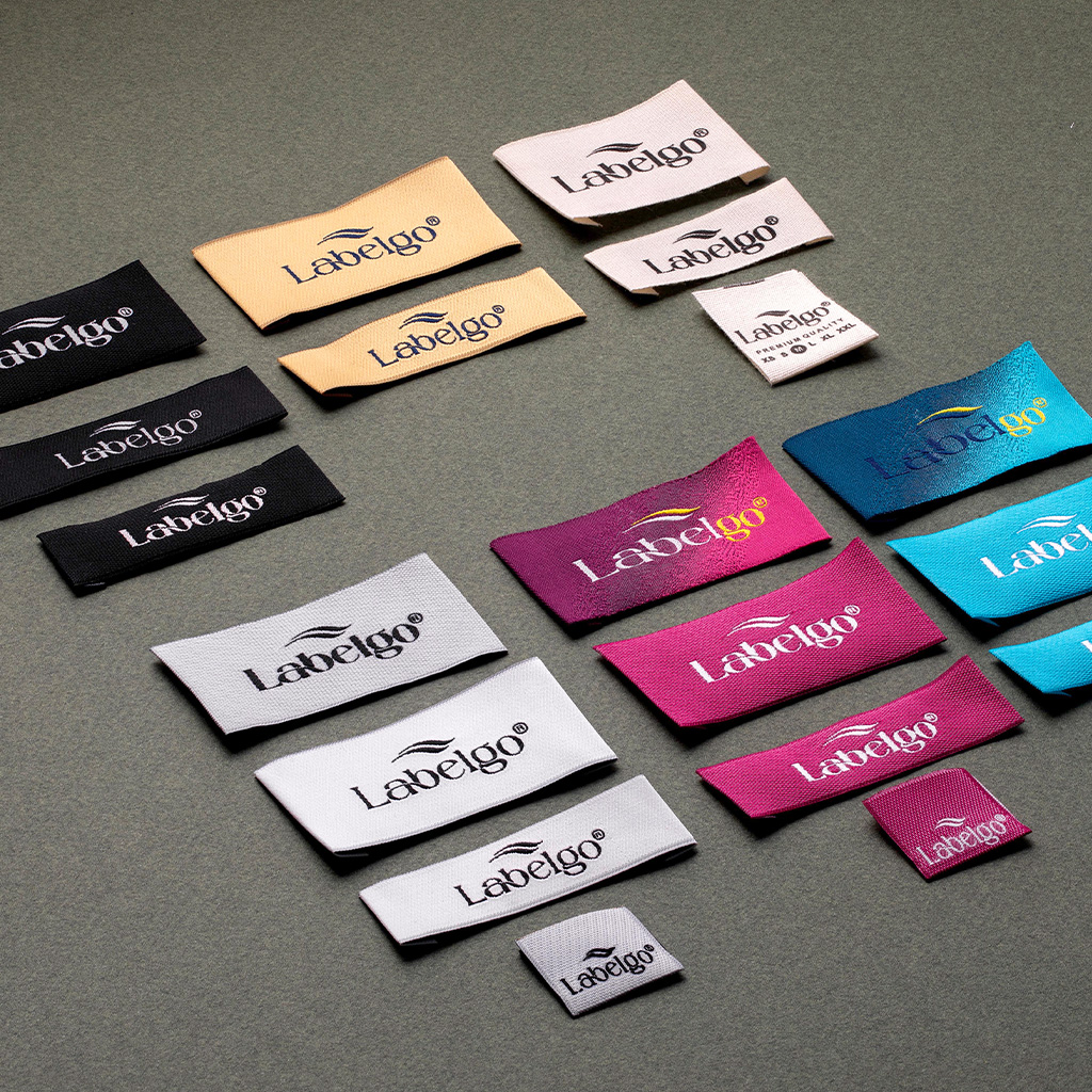 Assorted woven clothing labels in black, purple, and gold on grey background.